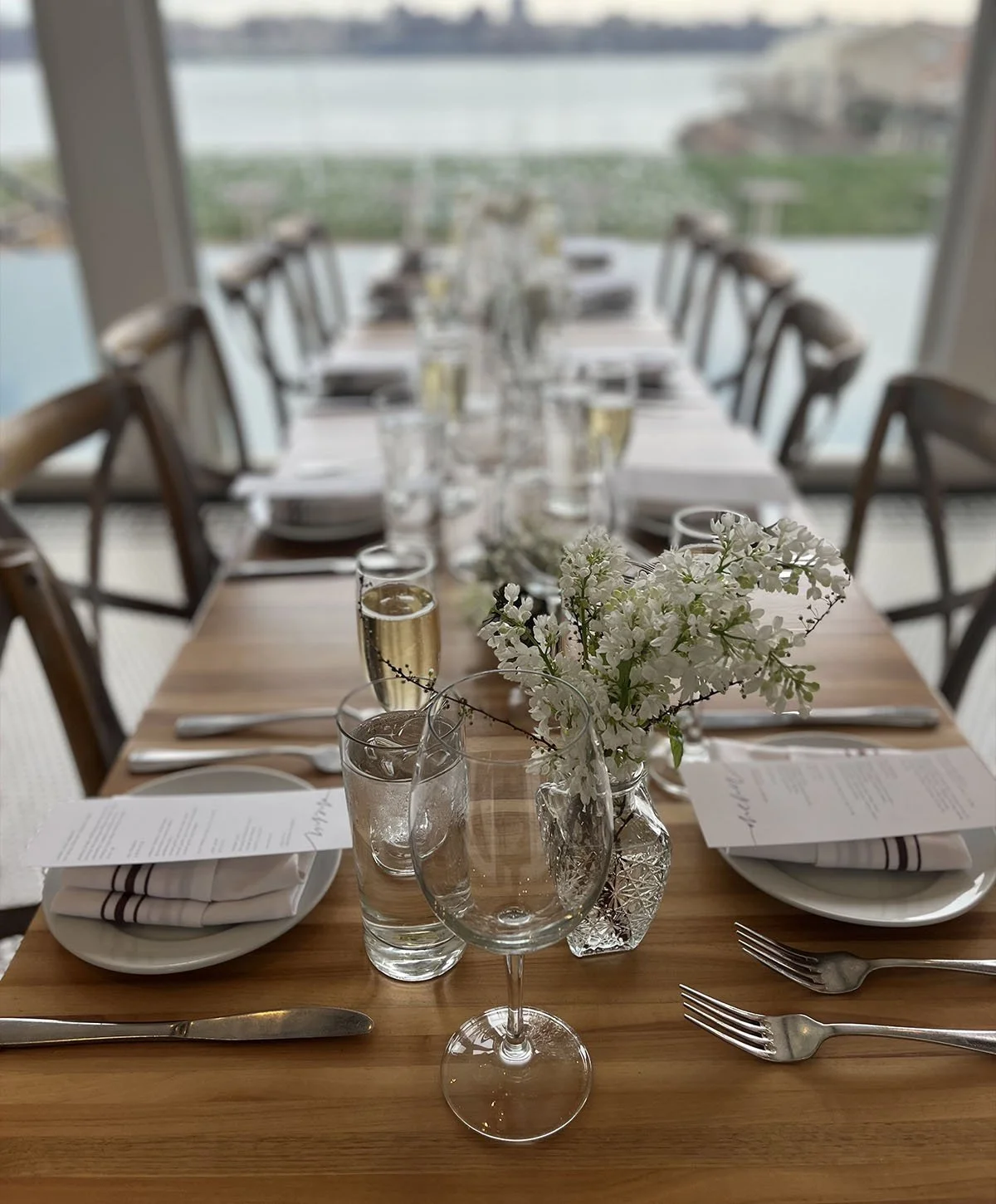 A long banquet table set for a private dinner at DeNovo Edgewater with the river view through the windows.