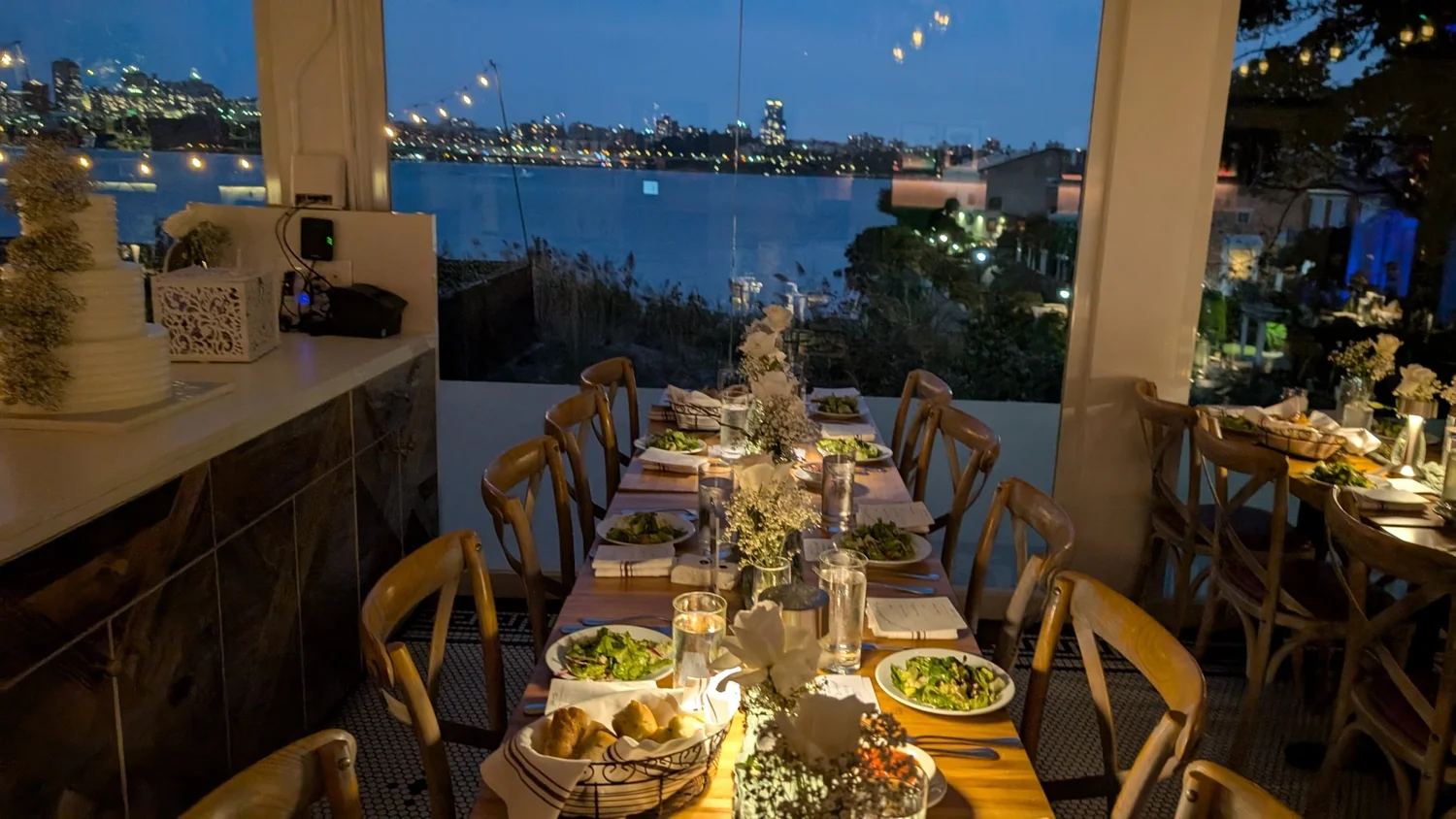 An evening wedding reception table by the window with the wedding cake and night skyline.