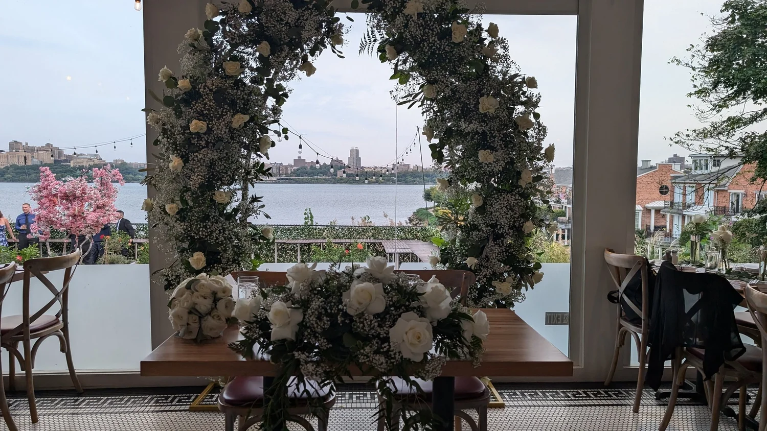 A wedding sweetheart table beneath a circular rose arch with the Hudson River behind.