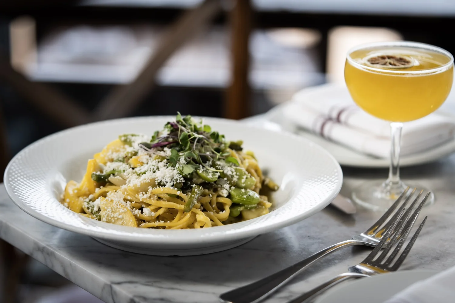 A plate of pasta beside a cocktail on a marble table at DeNovo Edgewater.