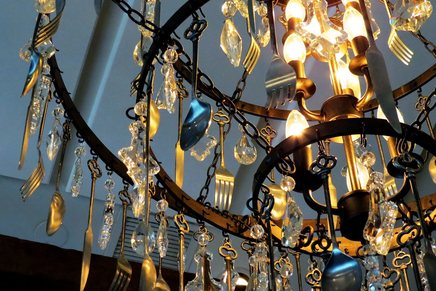 A decorative chandelier at DeNovo Edgewater made of crystals and gold forks and spoons.